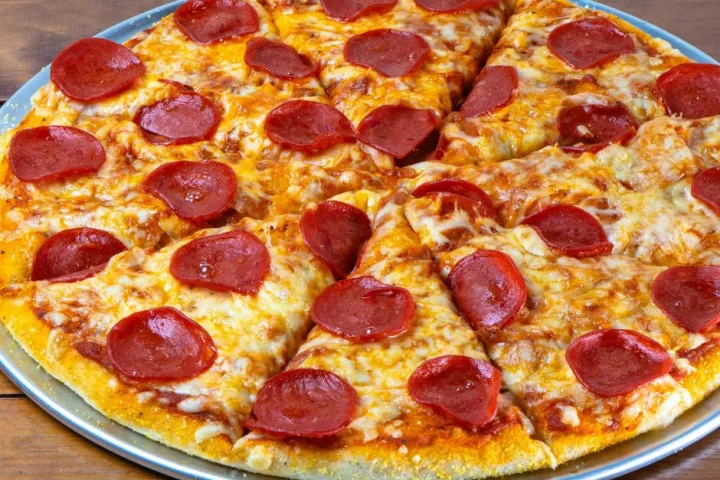 Pepperoni pizza on a metal tray with two slices slightly pulled apart.