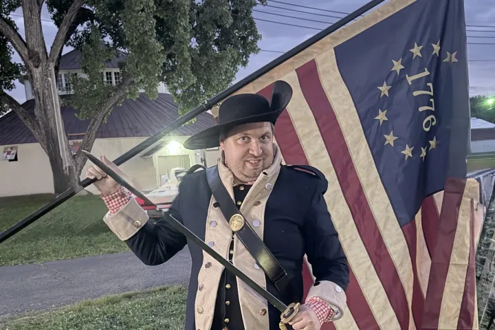 Man in colonial attire holding historical American flag outdoors.