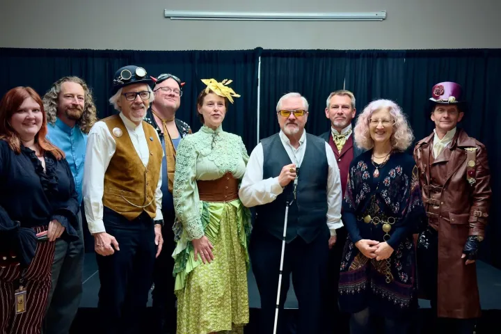 Group in steampunk attire with various costumes and accessories on a stage.