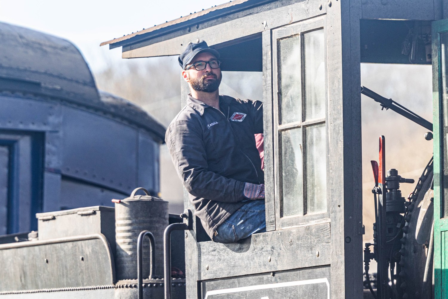 Man in glasses and cap driving a vintage train engine.
